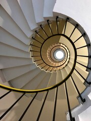 View looking up a spiraling staircase, highlighting its circular and symmetrical design. The railing curves inward, drawing attention to the architectural patterns and depth.