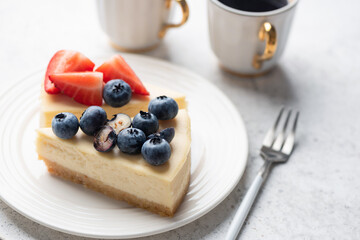 Cheesecake slice with strawberries and blueberries on white plate