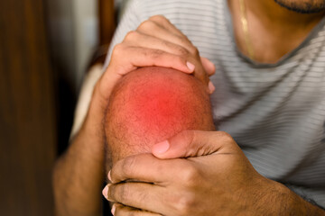 Man holding knee in pain at home during daytime