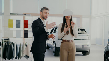Manager providing innovative method for selecting auto. Potential client using VR headset while choosing vehicle. Learning information about car model with high-tech. Modern customer interaction.