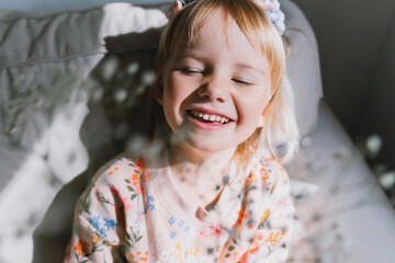Beautiful little girl smiling and squinting in sunlight. Portrait of dreamy playful child preschool...