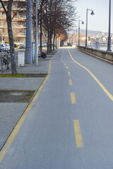 A bicycle lane marked with a yellow line runs along the sidewalk by the riverbank.