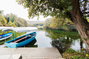 Traditional wooden boat with canopy floating on pristine water at Drim River Springs surrounded by...