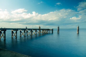 Clouds over a serene lake with a rustic wooden pier and smooth silky still blurred water
