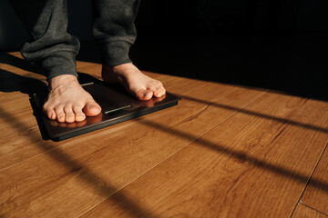 Man measuring her weight using scales on floor on a sunny morning. Man checking his weight on weight scale.
