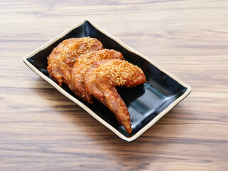 Glazed Chicken Wings sprinkled with sesame seeds served in black dish isolated on table side view...