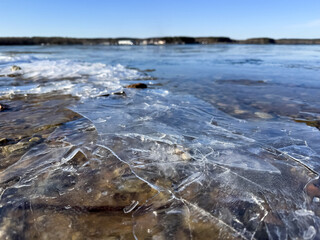 Cracked ice on a rocky shore of a thawed lake under a bright spring blue sky. A contrast of melting cold and warm seasonal renewal