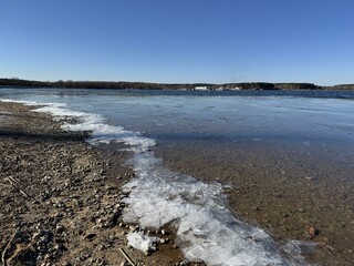 Cracked ice on a rocky shore of a thawed lake under a bright spring blue sky. A contrast of melting...