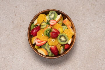 Fruit salad in wooden bowl on beige background. Kiwi, orange, strawberry, apple, pear top view