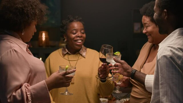 Cheerful Black woman raising toast then clinking glasses with extended family members while standing in circle in living room with warm soft light