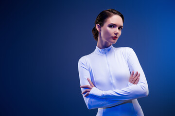 Stylish young woman in white sportswear posing with confidence in blue neon lighting embracing...