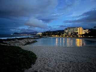 Fototapeta premium Ko Olina coastline on Oahu Hawaii on a cloudy evening, yellow lights reflecting off the water