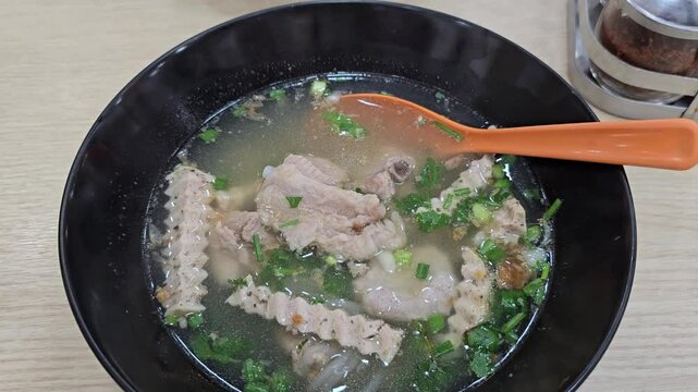 Asian food style : Vietnamese Rice Noodles Soup served in a black cup, orange spoon and have smoke rising from it  . Pho Bo ( Vietnamese Noodles) with coriander and chopped spring onions for extra fla