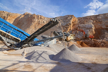 Stone crushing machine at open pit mining and processing plant for crushed stone. Piles of gravel stone and conveyor belts. Excavator loading rocks. Concepts of industry and building materials