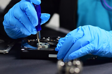 A technician in a hard disk assembly lab is disassembling and repairing a hard disk on a workbench, wearing gloves and holding a screwdriver to repair the hard disk or recover data.