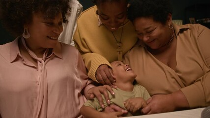 Medium shot from festive dining table of happy Black family playing with little boy touching kids nose at home celebration, handheld camera