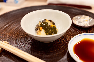 Abalone sashimi topped with sea urchin, elegantly served in a ceramic bowl with soy sauce on the side