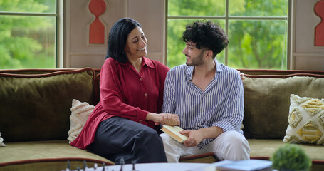 Indian happy mature woman lady with young man male sitting on cozy sofa couch talk gossip share...