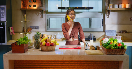 Indian young adult gen z woman lady use mobile talk phone call distant enjoy day time have fun joy teen age girl hold mobile speak gossip indoor modern kitchen	