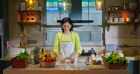 Indian asian gen x woman lady chef wear apron knead flour with hand indoor modern kitchen spend...