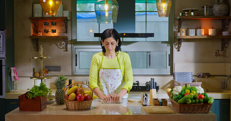 Indian asian gen x woman lady chef wear apron knead flour with hand indoor modern kitchen spend time young adult alone female mother mom bake food pastry dough bread on counter table enjoy day house