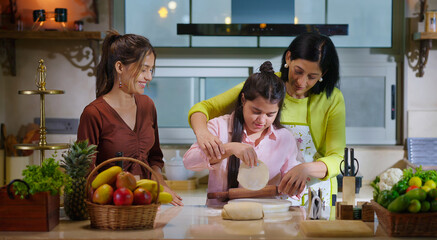 Indian happy young woman lady with cute teen cute girl hold roller rolling raw flour dough learn cook food indoor home adult mom teach kid child trying to bake cookies enjoy day modern home kitchen
