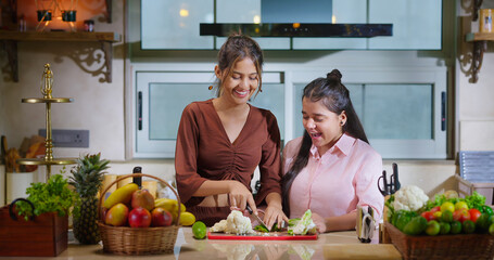 Indian young adult gen z woman lady teach cut fresh vegan slice on chop board to teen age girl...