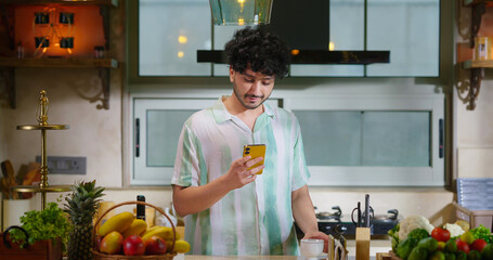 Indian young adult gen z man guy use mobile look chat online app read new text SMS email indoor...