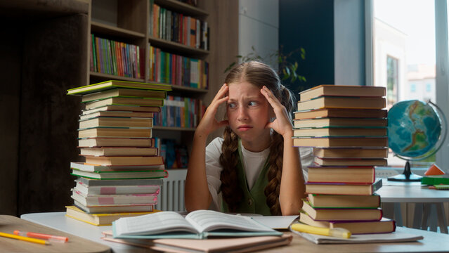 Bored annoyed angry suffering Caucasian little girl school child kid schoolgirl learning hard schoolwork books too much homework struggle education problems mental burnout exhaustion indoors library
