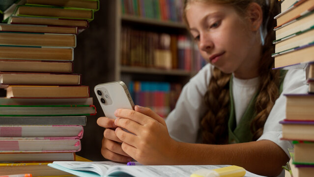 Little girl Caucasian bored school child kid teenage learner unmotivated student pupil schoolgirl boredom use mobile phone chat online smartphone social media education lesson indoor classroom library - Powered by Adobe