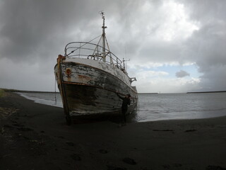 A woman near a Timeworn and rusted, this stranded shipwreck stands resilient against Iceland’s...