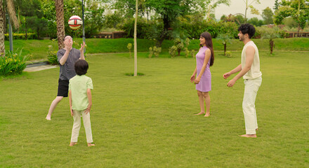 Naklejka premium Indian happy active family group playing casual foot ball game enjoy outdoor garden park middle aged older dad spend day with cute teen child kids son young adult girl boy have fun joy sports time