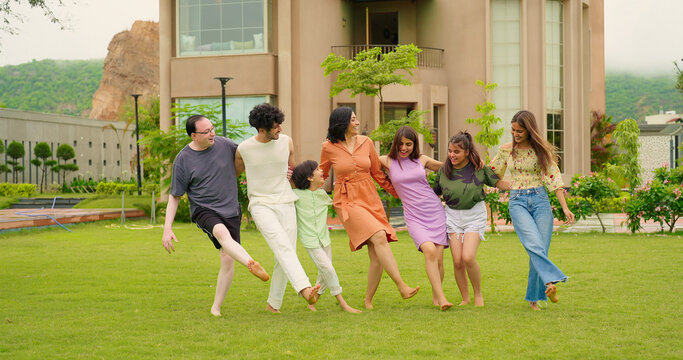 Indian happy family group dancing with teen girl child cute son kid boy enjoy day outdoor home park. Adult mom dad man woman young male female have fun joy play game spend time at outside garden house