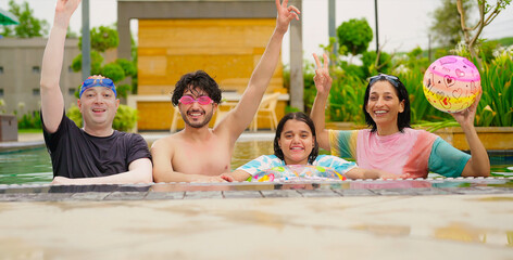 Indian happy family group with teen child dancing look cam enjoy outdoor resort pool edge trip mom dad young adult girl boy make female do pose have fun joy spend day time at outside water park	
