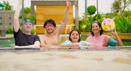 Indian happy family group with teen child dancing look cam enjoy outdoor resort pool edge trip mom dad young adult girl boy make female do pose have fun joy spend day time at outside water park