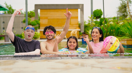 Indian happy family group with teen child dancing look cam enjoy outdoor resort pool edge trip mom dad young adult girl boy make female do pose have fun joy spend day time at outside water park