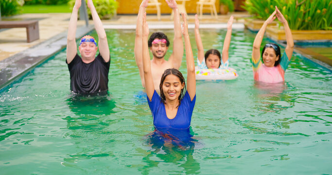 Indian happy wet family male female lady man group do warm up exercise in pool enjoy day outdoor water park resort trip picnic young mom dad with cute teen girl child adult boy have fun joy spend time - Powered by Adobe