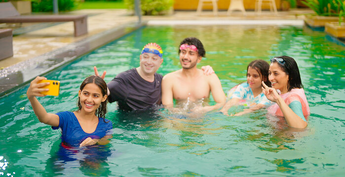 Indian happy wet cute teen girl boy young mom hold mobile look cam take selfie make pose water pool resort mom dad adult child use phone record shoot video spend time have fun joy outdoor hotel trip