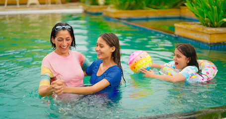 Indian middle aged relax woman teen girl dancing in pool enjoy resort water park happy elder active wet mom lady playing ball with young adult cute child have fun joy spend time at luxury outdoor trip
