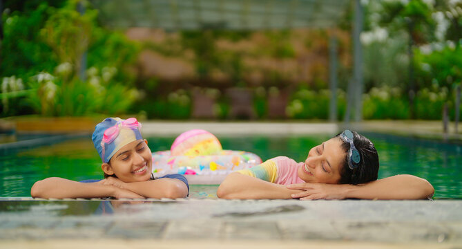 Indian relax wet adult mom woman with cute teen girl standing take rest on pool edge feel tired. Two young female talk gossip at outdoor water park resort trip spend time luxury hotel villa enjoy day