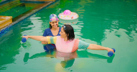 Indian happy mom with teen age girl standing do self body health care warm up arm stretch in pool. Mature woman lady young adult child enjoy trip day have fun joy spend time at water park resort