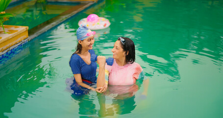 Indian happy mom with teen age girl standing do self body health care warm up cross arm stretch in pool. Mature woman lady young adult child enjoy trip day have fun joy spend time at water park resort