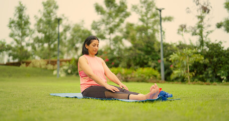 Indian mature adult older gen x woman lady sitting on yoga mat do stretch warm up toe touch asana...