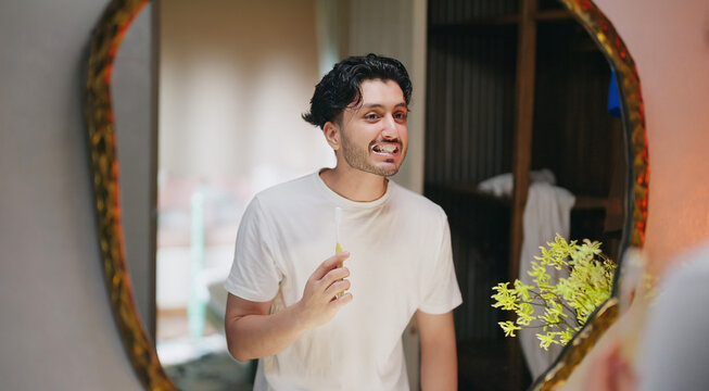 Indian young adult gen z alone smiling man guy look mirror do morning day dental care daily routine indoor home teen age male boy hold brush clean mouth remove gum healthy white teeth good habit