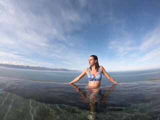A woman enjoys the breathtaking tranquility of a natural hot spring, where crystal-clear waters reflect the endless Icelandic sky in complete serenity.
