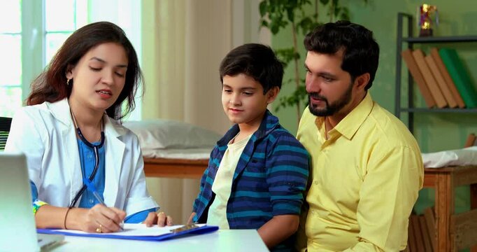 Indian woman doctor writing prescription for young boy with father during checkup at modern clinic, ensuring proper diagnosis and professional healthcare guidance