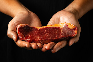 A pair of hands presenting a fresh raw steak against a dark background