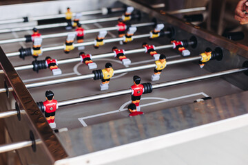Group of friends playing kicker in a sports bar room, colleagues teammates play table football,...