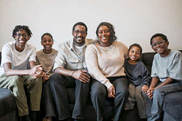 Portrait of happy black family sitting at home. Smiling couple with kids sitting on couch.