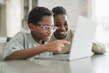 Little American boy studying online with laptop in kitchen with sister